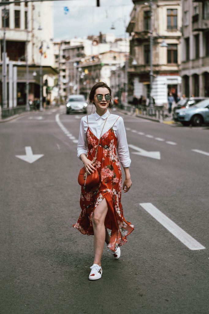 woman crossing street with a red dress over a white button-down shirt