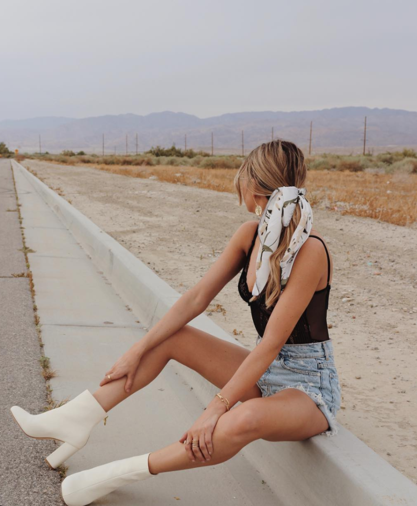 Woman wearing white boots on the side of the road.