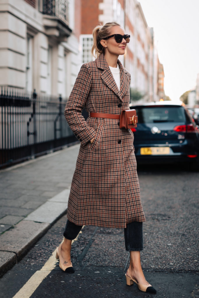 Woman wearing long plaid overcoat outside, synonymous with fall styles.