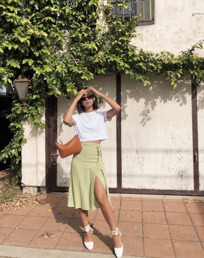 woman wearing cropped white tee with a soft green midi skirt.