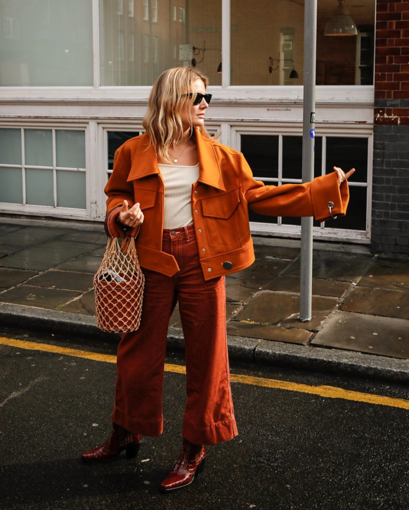 Woman wearing orange jacket with red pants and accessories.