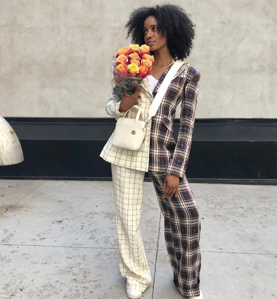 Photo of Naomi holding flowers in a suit with multiple patterns.