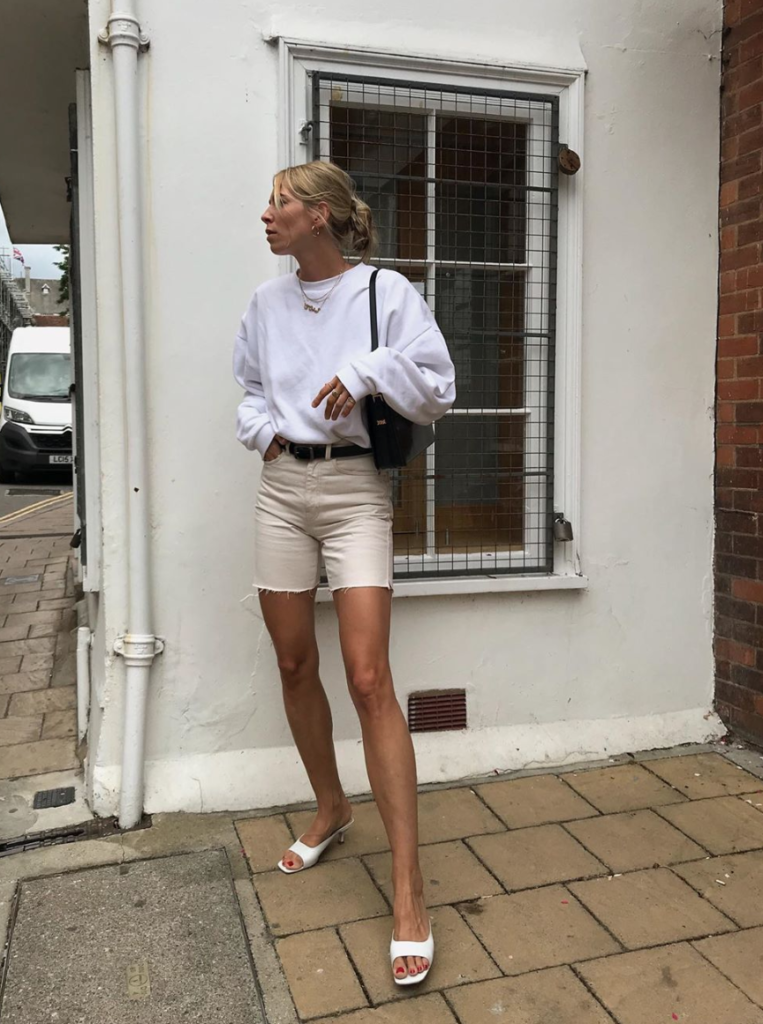 Woman wearing denim shorts and white crewneck for fall transition style.