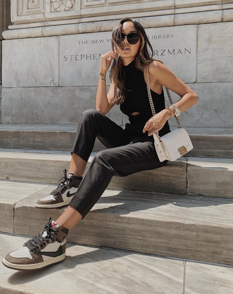 Blogger wearing darker neutrals with sneakers sitting on outside stairs.