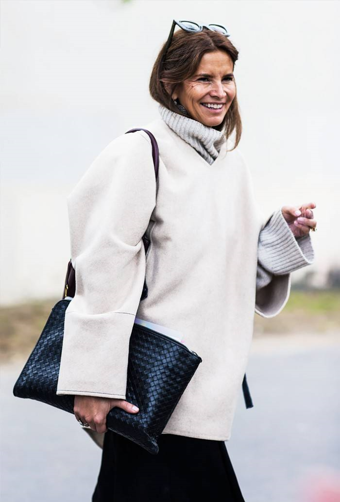Woman layering two sweaters over one another with black purse.