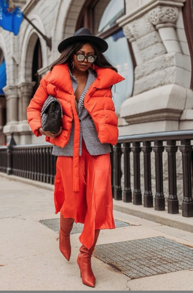 Woman layering clothes underneath an orange puffy coat.