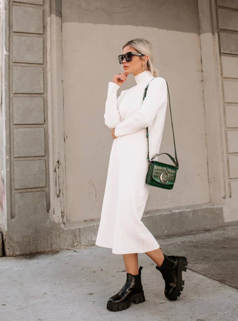Blogger wearing a mock neck knitted dress with green bag and black boots.