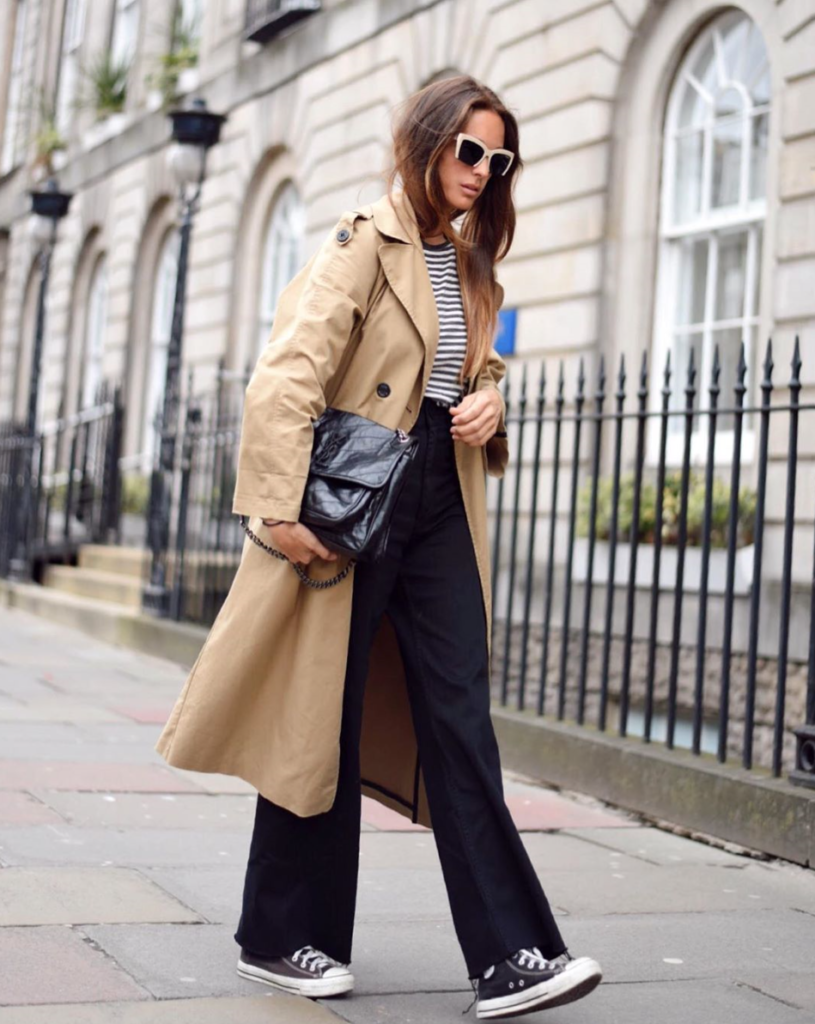 Woman pairing flared pants with beige trench coat.