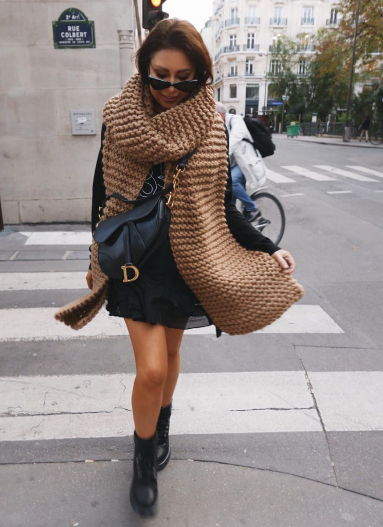 Woman wearing oversized scarf and leather purse.