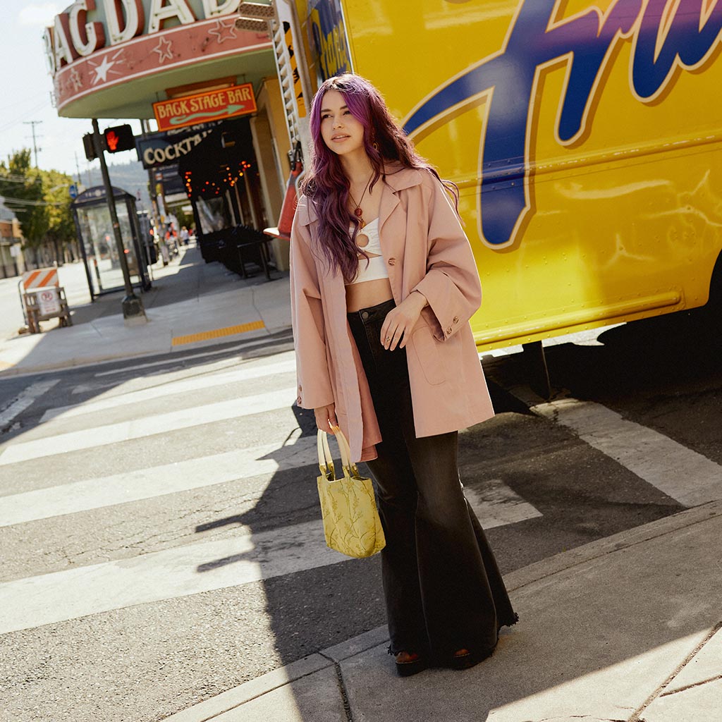 Model in pink jacket holding yellow bag.