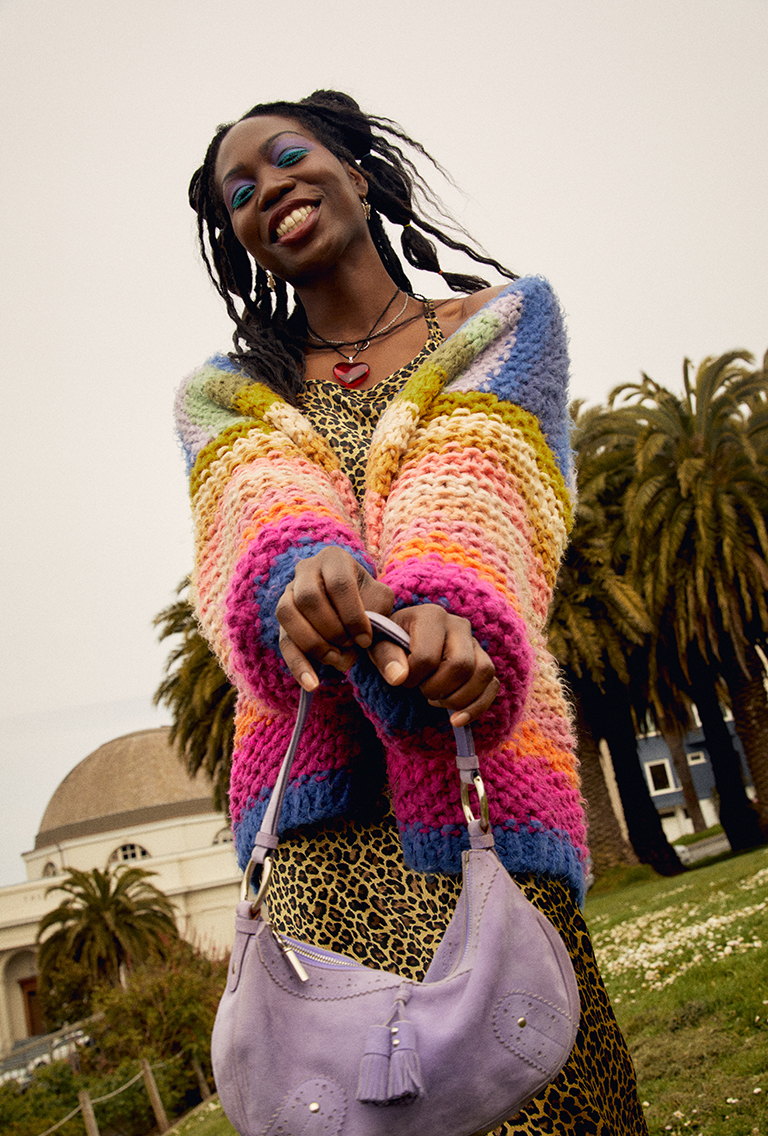 Model wearing rainbow cardigan holding a purple purse