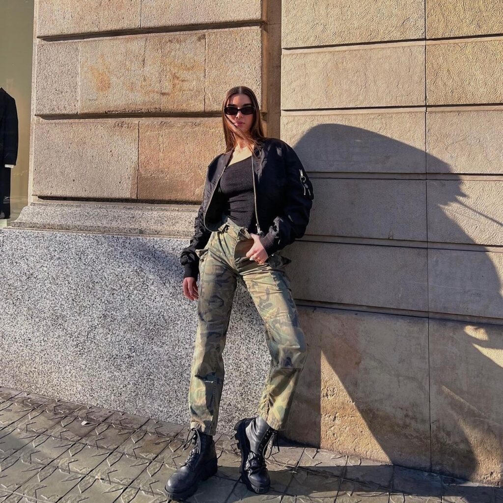 photo of person wearing camo-print pants with black combat boots and black bomber jacket