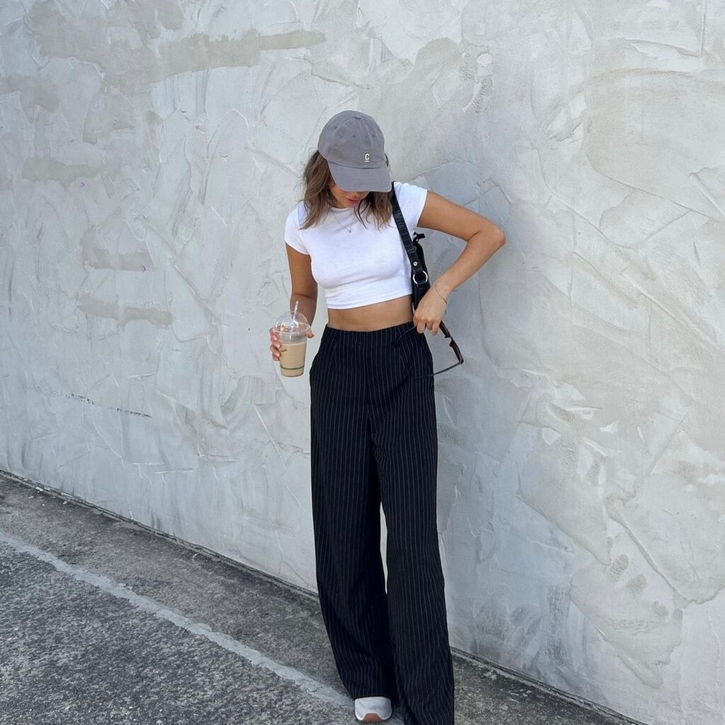 woman dressed in white crop top, baseball camp, and pinstripe pants