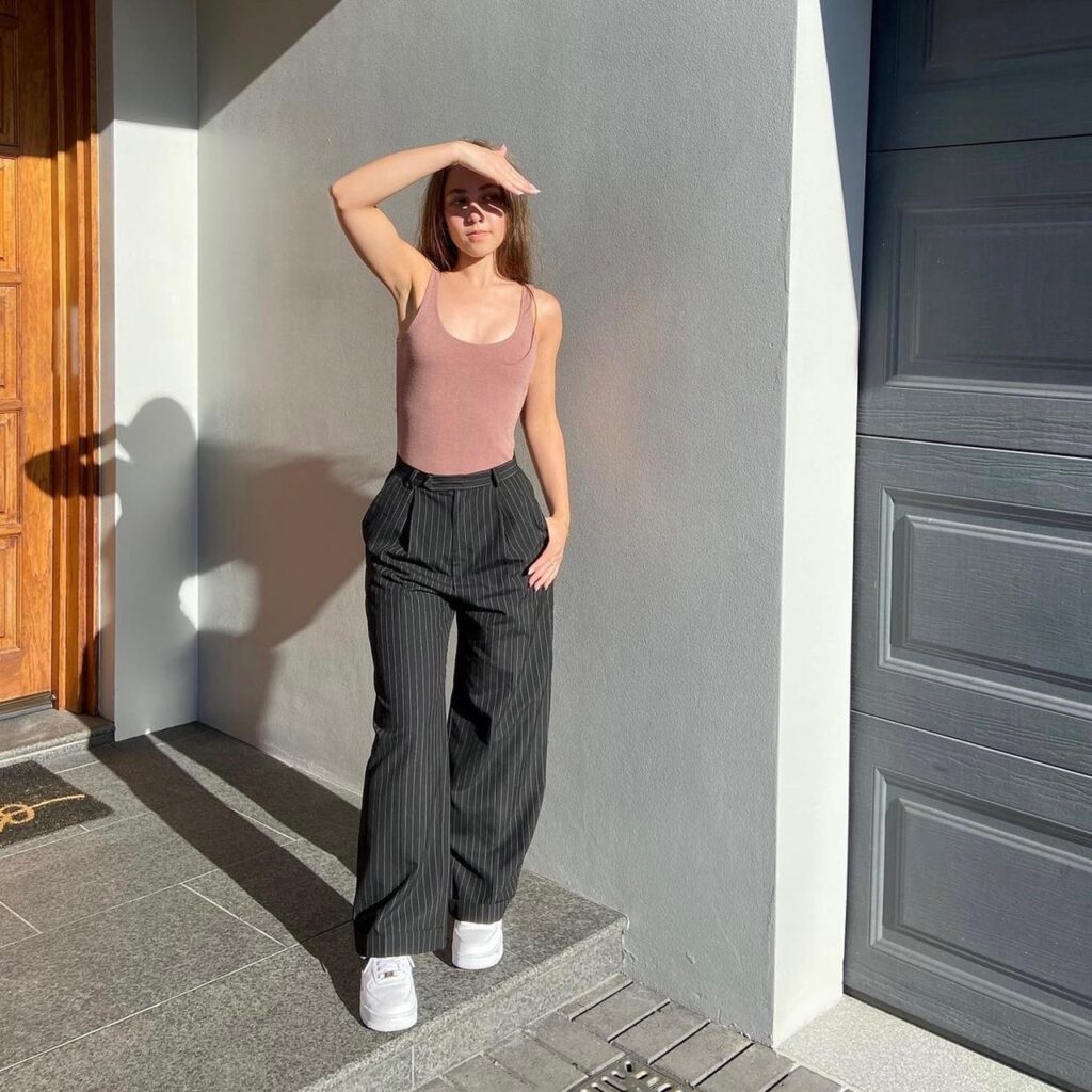 woman wearing blush-colored tank top and baggy charcoal-colored trousers