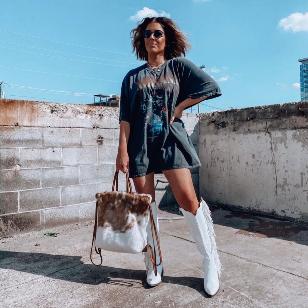woman in oversized graphic tee with knee-high white boots and cowhide handbag