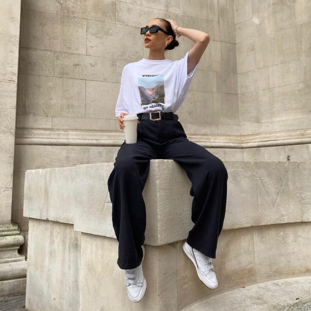 woman earing a t-shirt tucked into black trousers, with white sneakers and sunglasses
