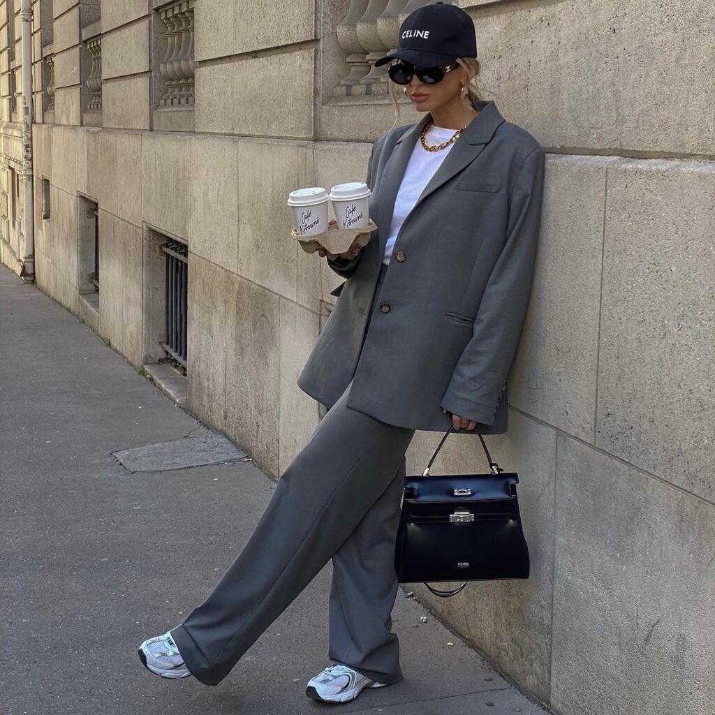 woman wearing a gray oversized suit with black cap and black handbag