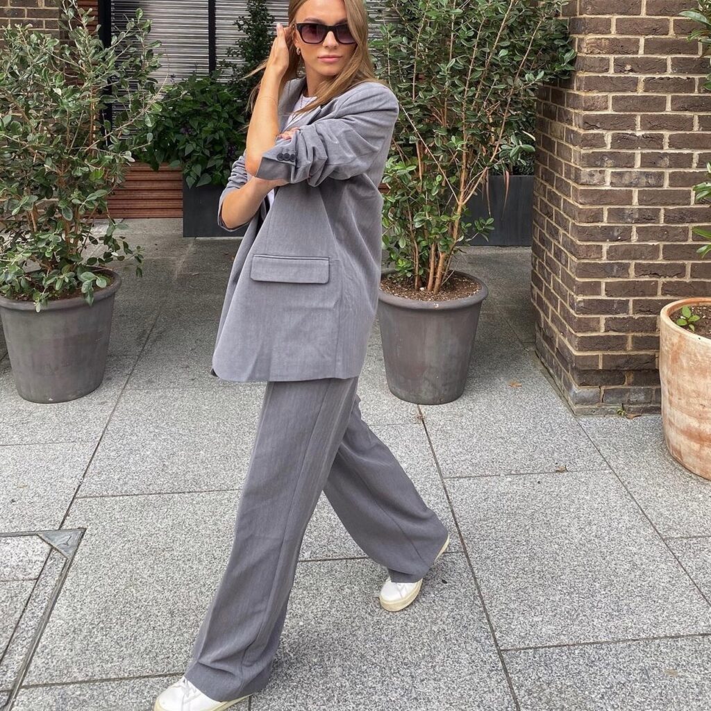 woman wearing a gray oversized suit with sunglasses and sneakers