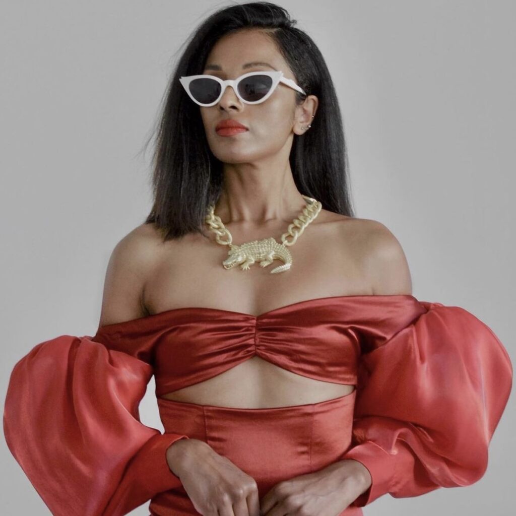 woman wearing white sunglasses, a red satin dress, and gold alligator necklace