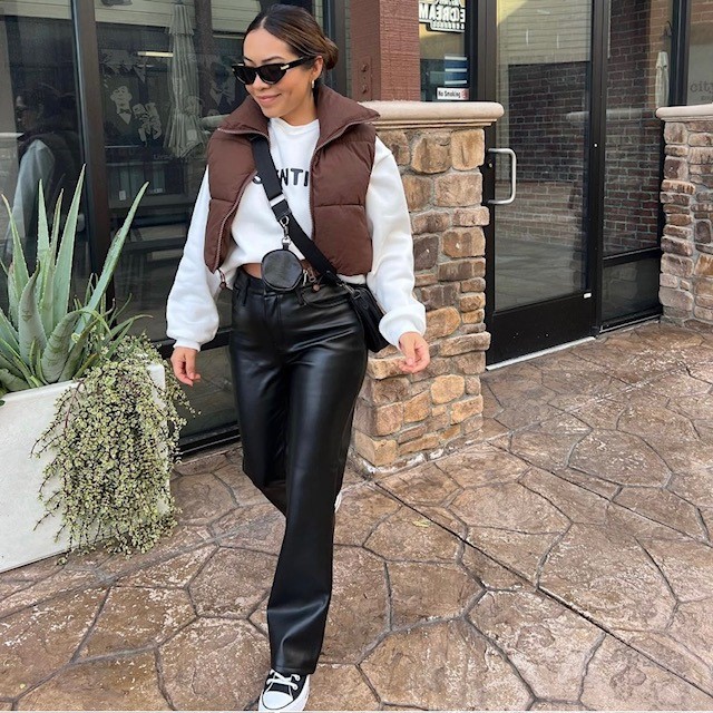 woman wearing cropped puffer vest over cropped sweatshirt with faux leather pants and sneakers