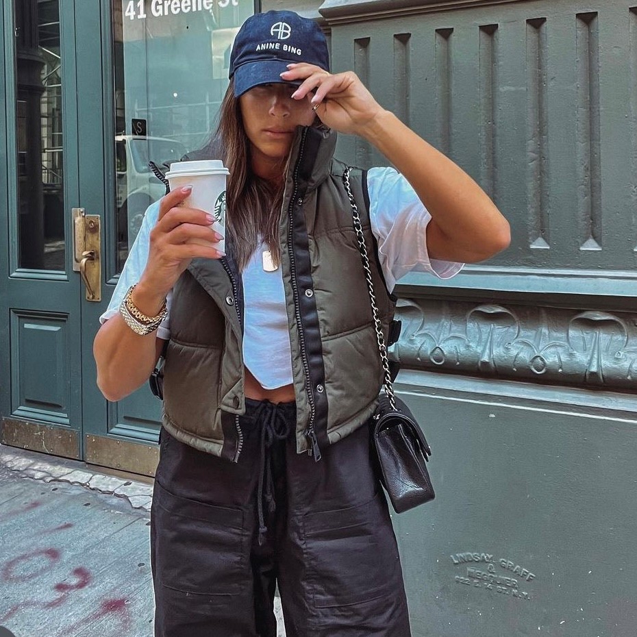 woman wearing puffer vest, cropped tee with cargo pants, and baseball cap