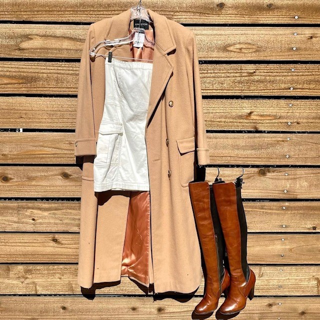 example of thrift store fashion pieces, like a wool coat, tall brown leather boots, and a cream-colored dress