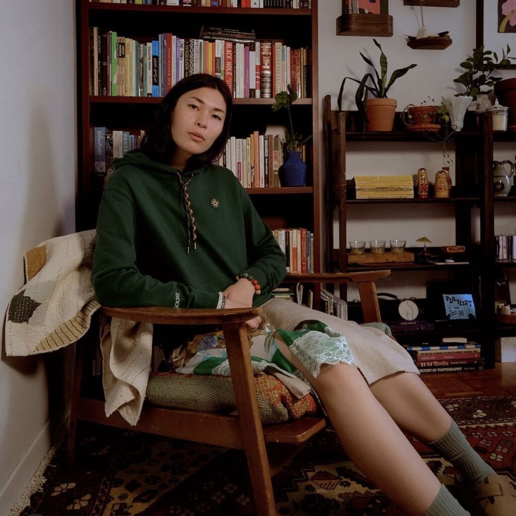 woman sitting in a chair with a green sweatshirt and mixed print skirt