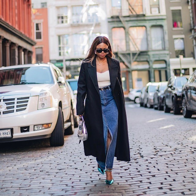 woman in long denim skirt with black trench and green metallic heels