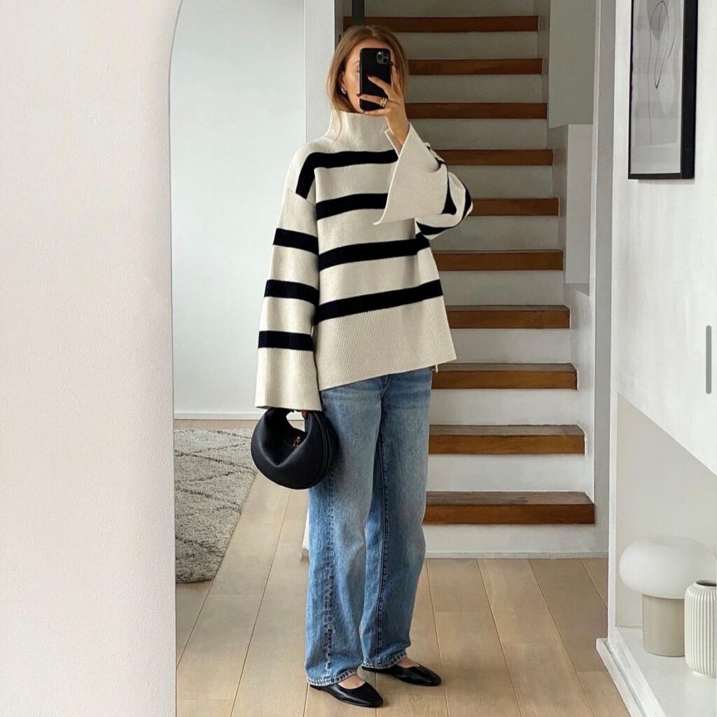 a woman wearing an example of a casual New Year's Eve outfit, an oversized striped sweater with relaxed jeans and ballet flats