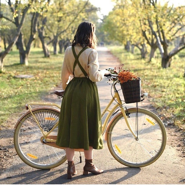 woman standing in an orchard with a bike