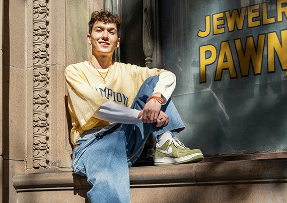 Model wearing yellow shirt and blue jeans sitting on a ledge