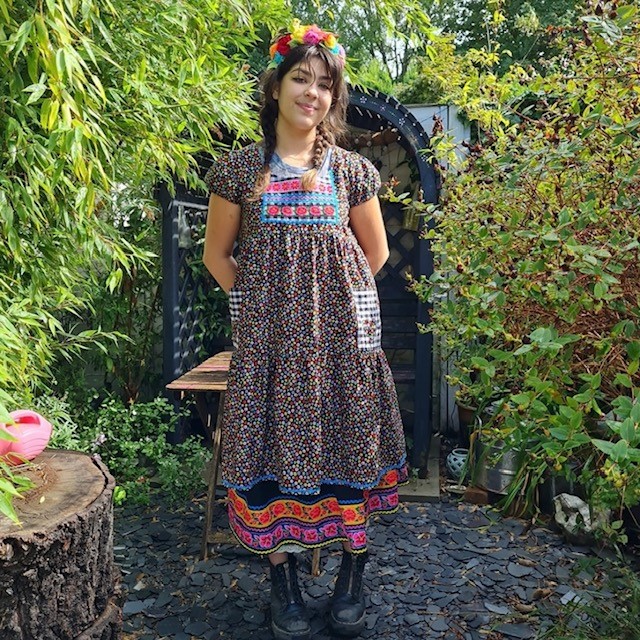 woman in black, pink, orange, and teal ditsy floral dress in an apron style