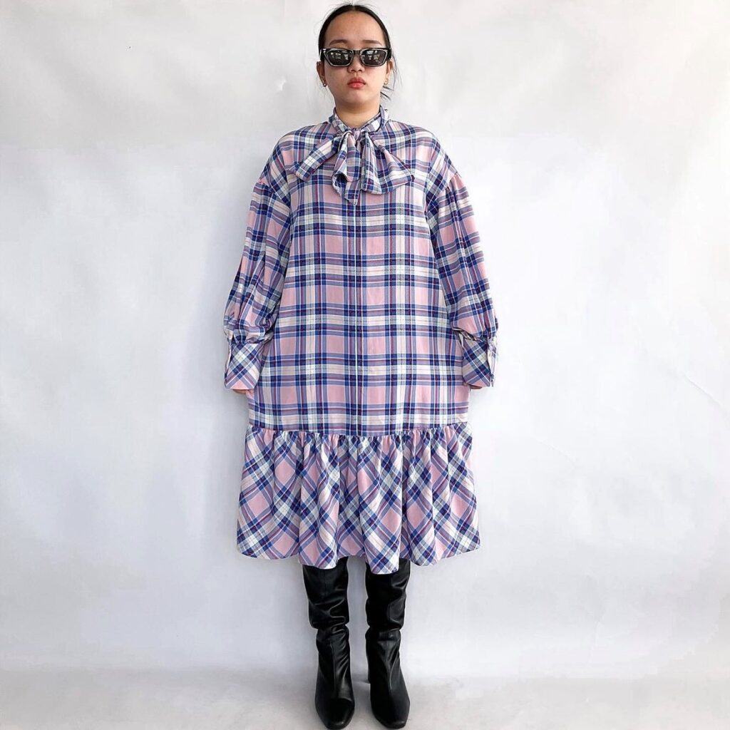 Woman wearing an example of flirty hemlines. A pink and purple plaid bow dress with frilly hem