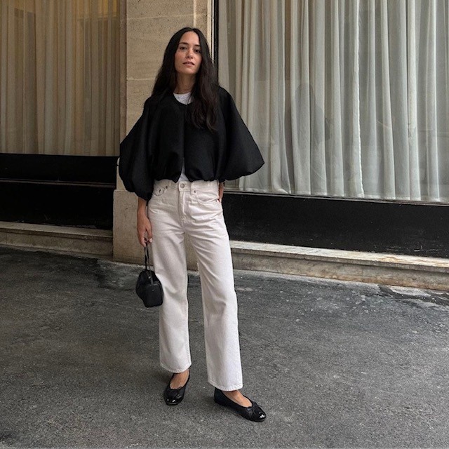 woman with black cape jacket, white jeans, and ballet flats