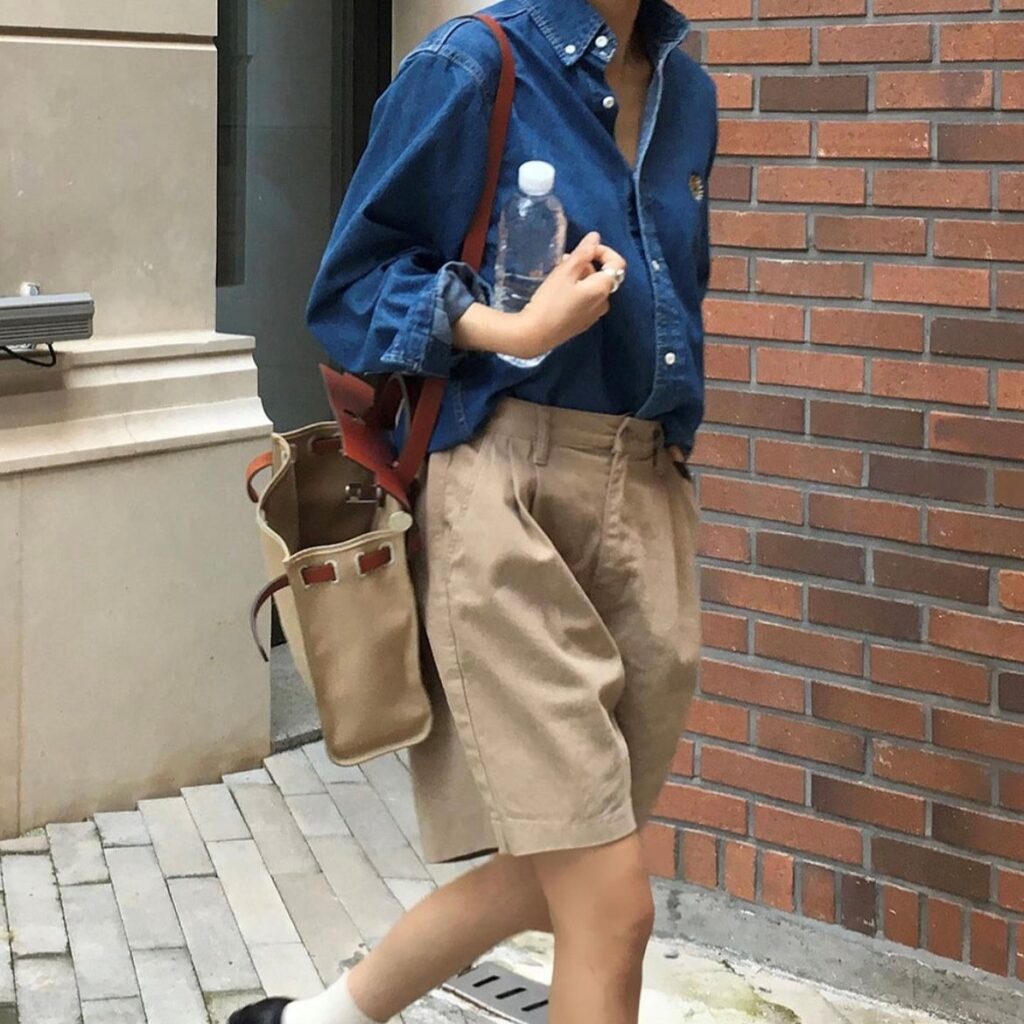 person in denim shirt and long pleated shorts