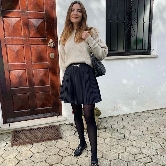 woman in cream colored sweater and black mini skirt with black tights and loafers
