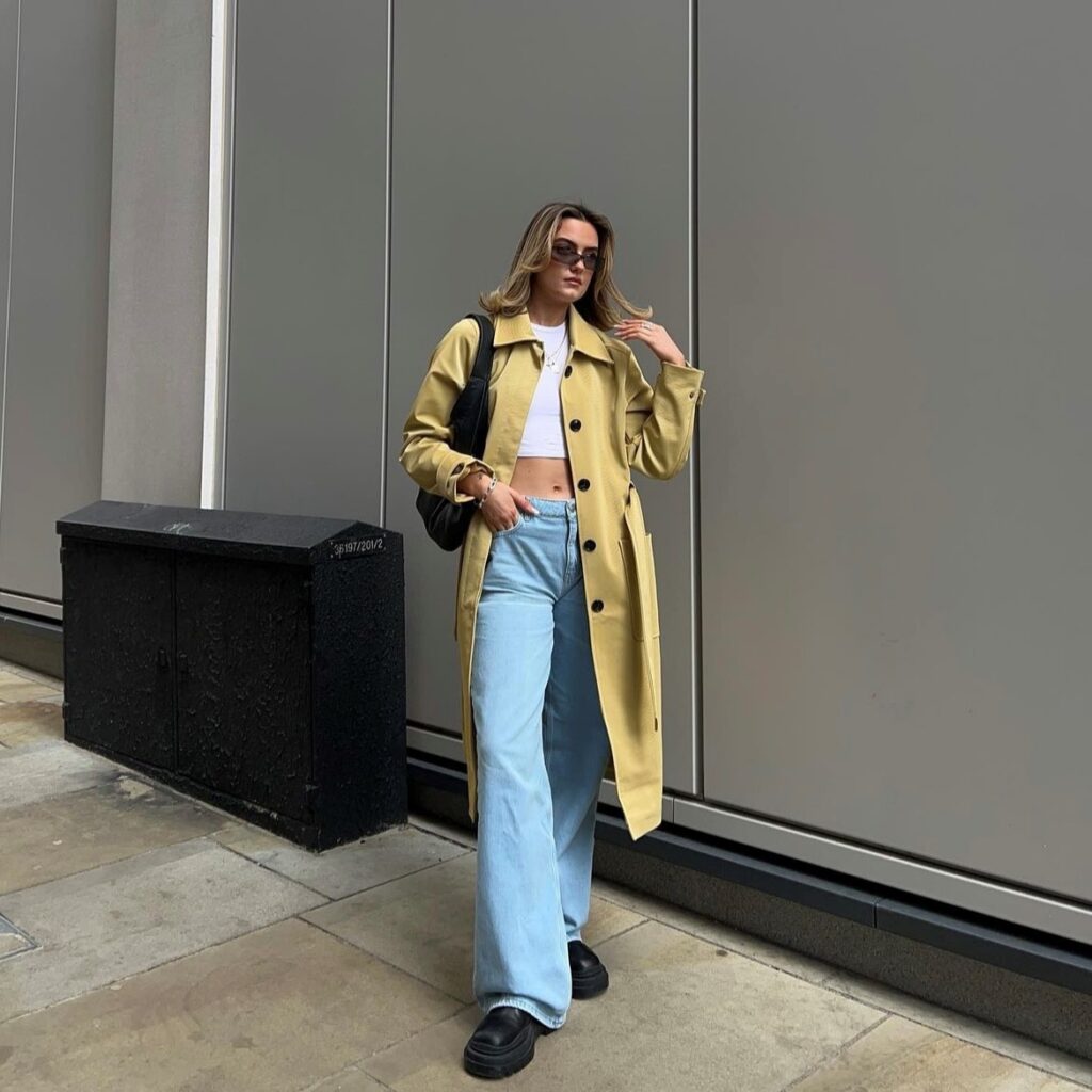 woman wearing puddle jeans with white crop top and trench coat