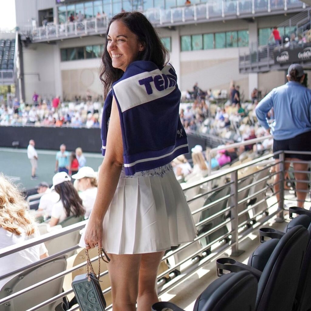 woman at a tennis match in a tenniscore look of white pleated skirt and sweatshirt