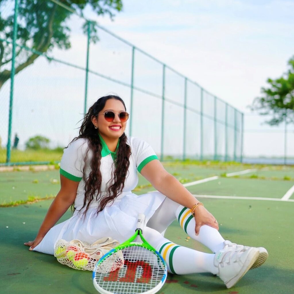 woman sitting on tennis court with polo shirt, tennis skirt, and knee-high sports socks
