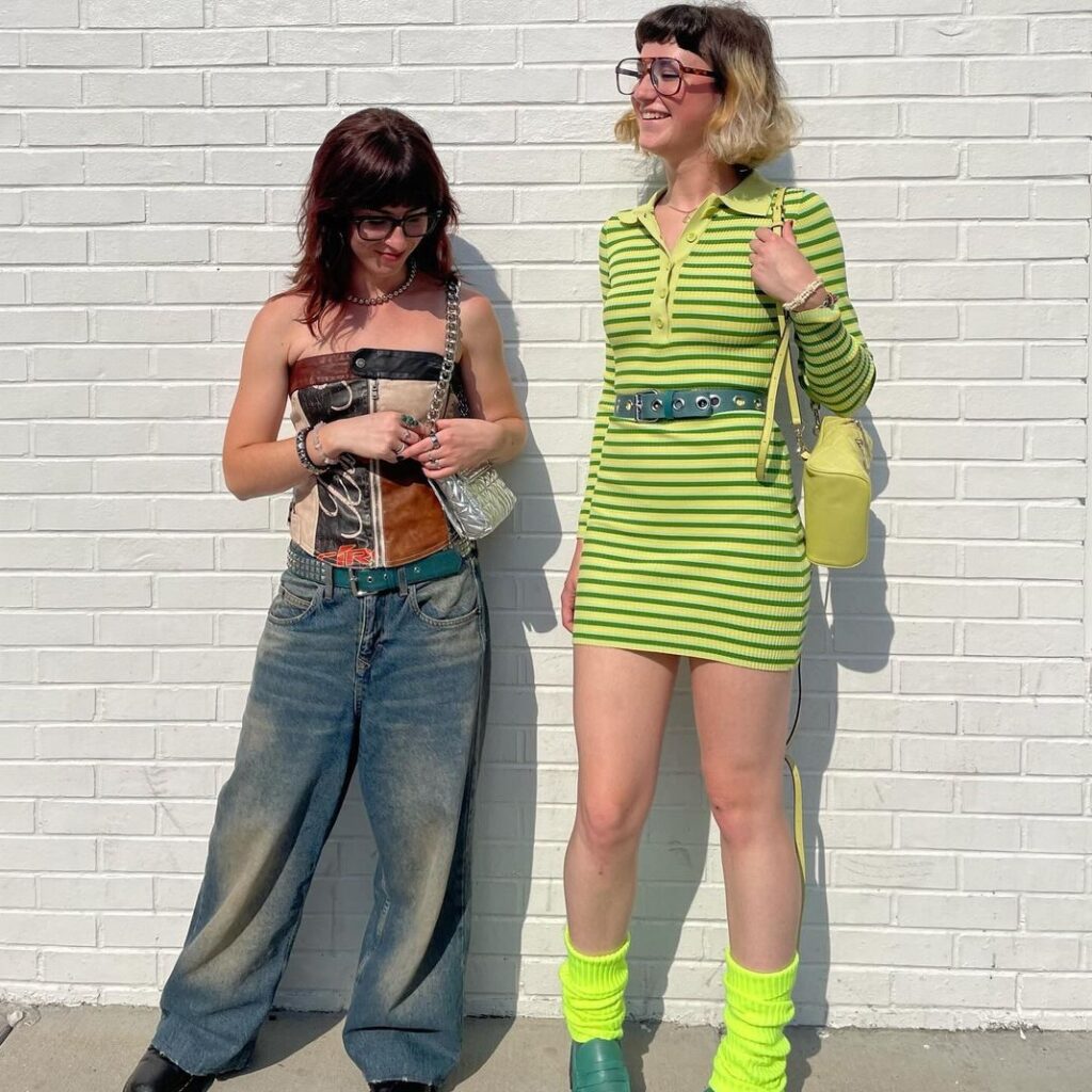 Two fashionable women standing in front of a white wall enjoying the sun