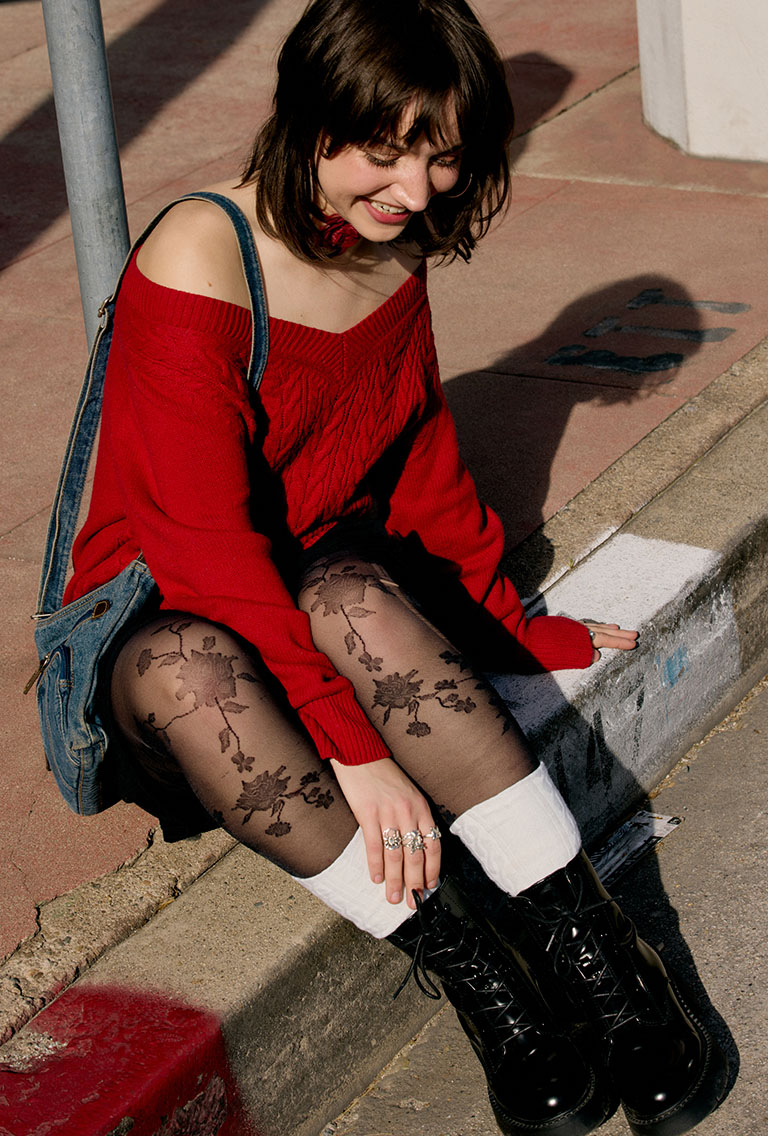 Model sitting on the curb wearing a red off shoulder sweater lettings and a rose necktie