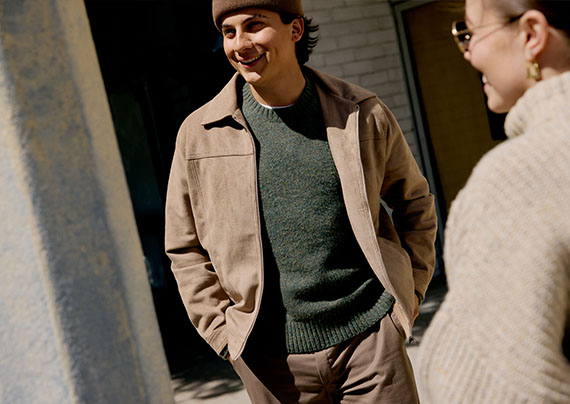 Male Model wearing tan jacket, green sweater, and beige pants