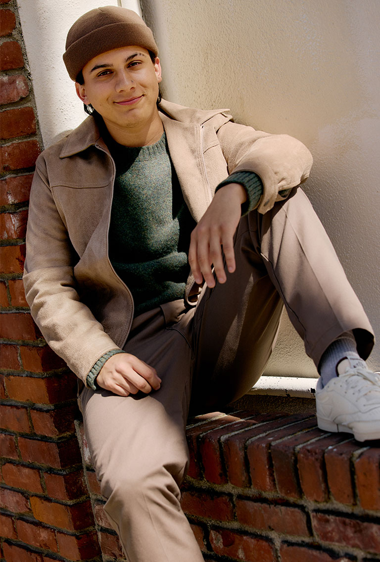 Male Model wearing tan jacket, green sweater, and beige pants