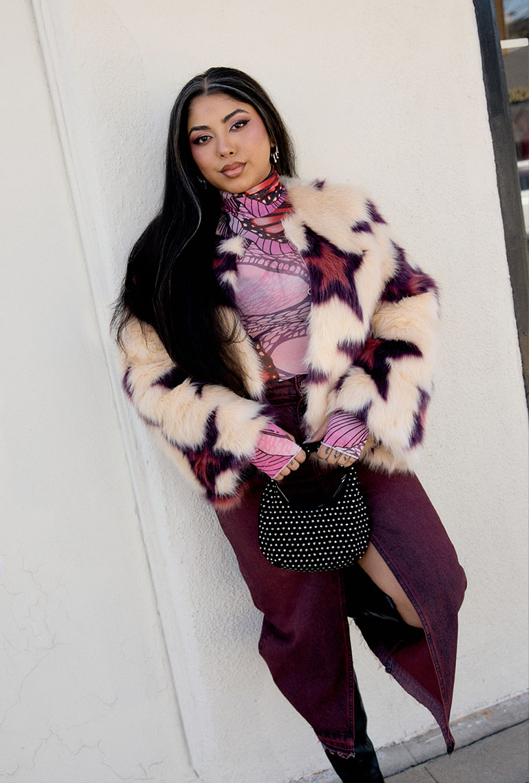 Model wearing cream faux fur jacket with pink stars, burgundy skirt and black boots