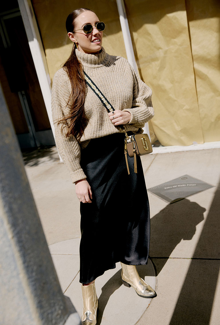 female model wearing beige sweater, black midi skirt, and a marc jacobs black and gold purse