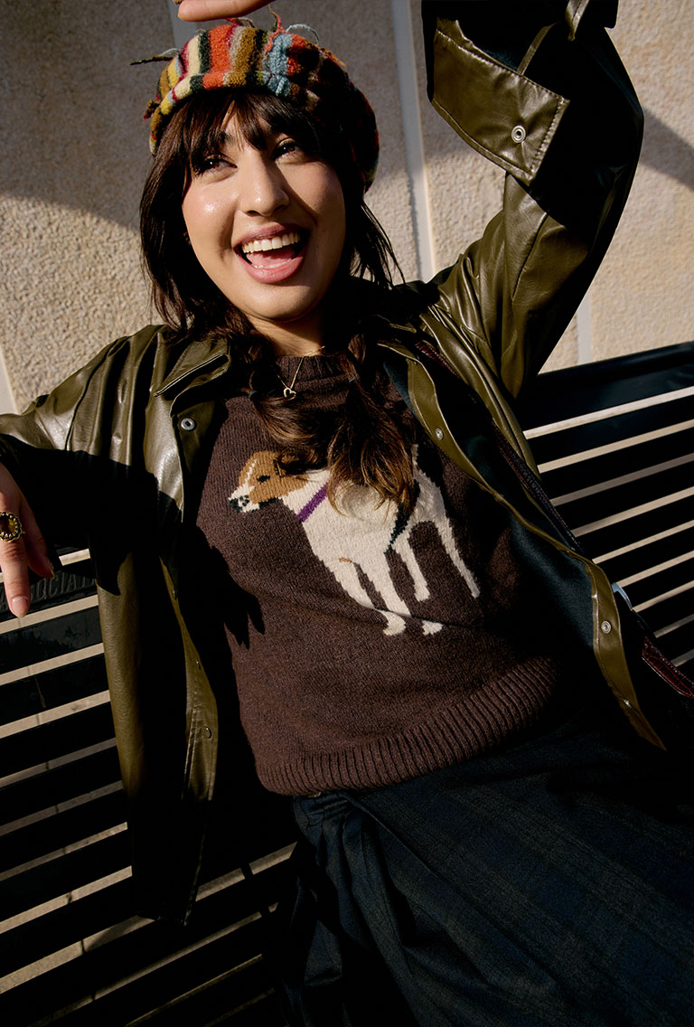 model wearing a rainbow knit hat, dog sweater, green leather jacket and a plaid skirt