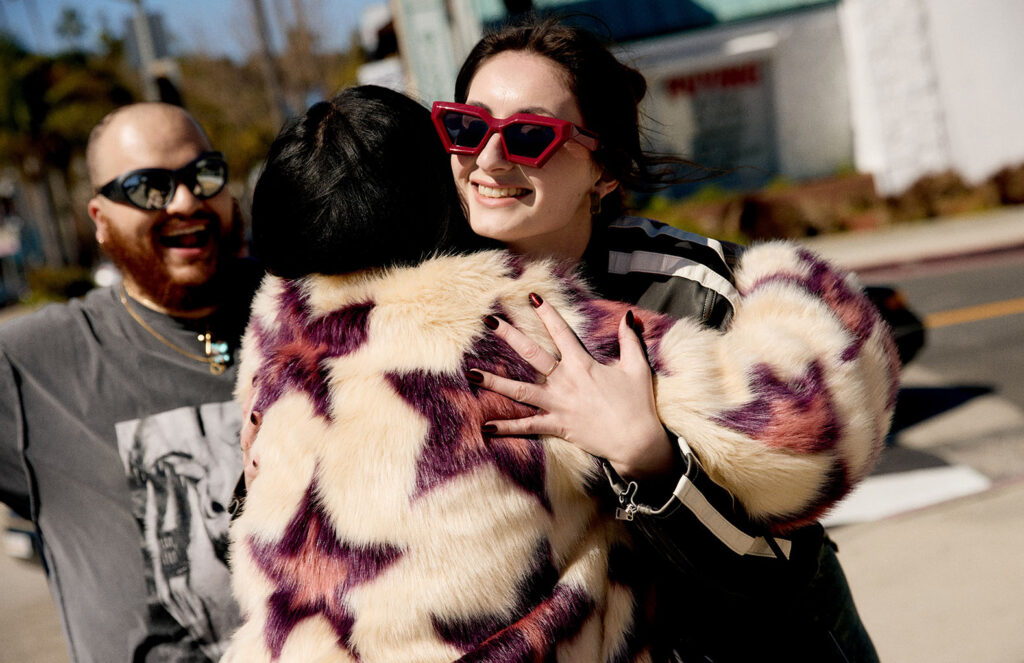 Mila wearing red sunglasses hugging kiko who is wearing a cream furry jacket with pink stars on it