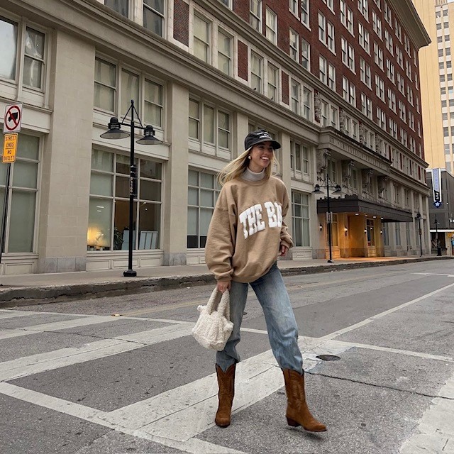 woman wearing cowboy boots with light wash jeans and oversized sweatshirt