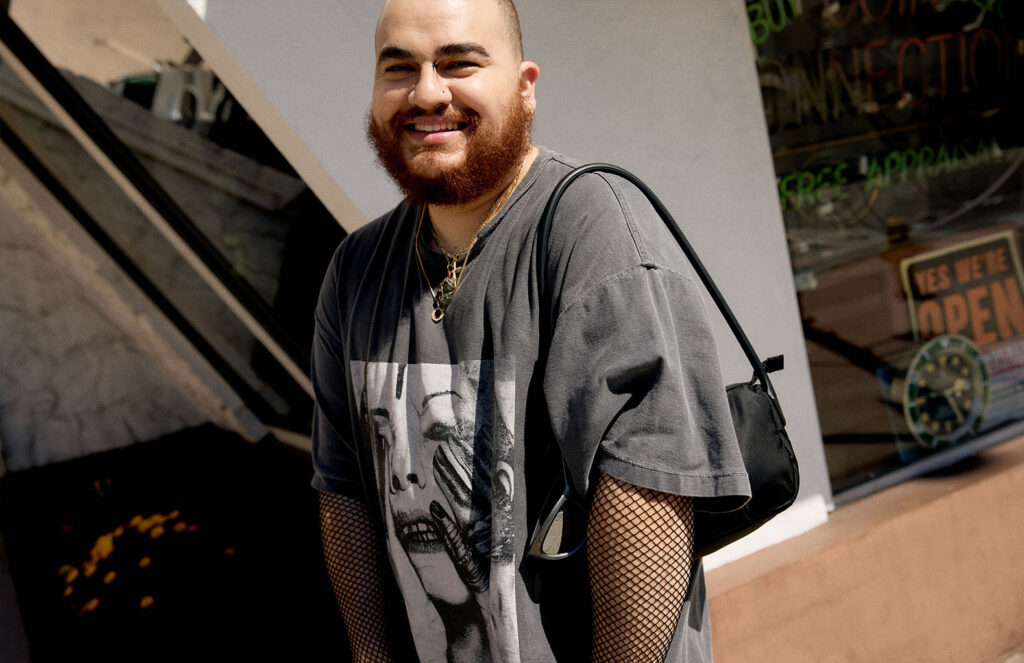 Nelson wearing sunglasses, fishnet sleeves and a graphic tee shirt