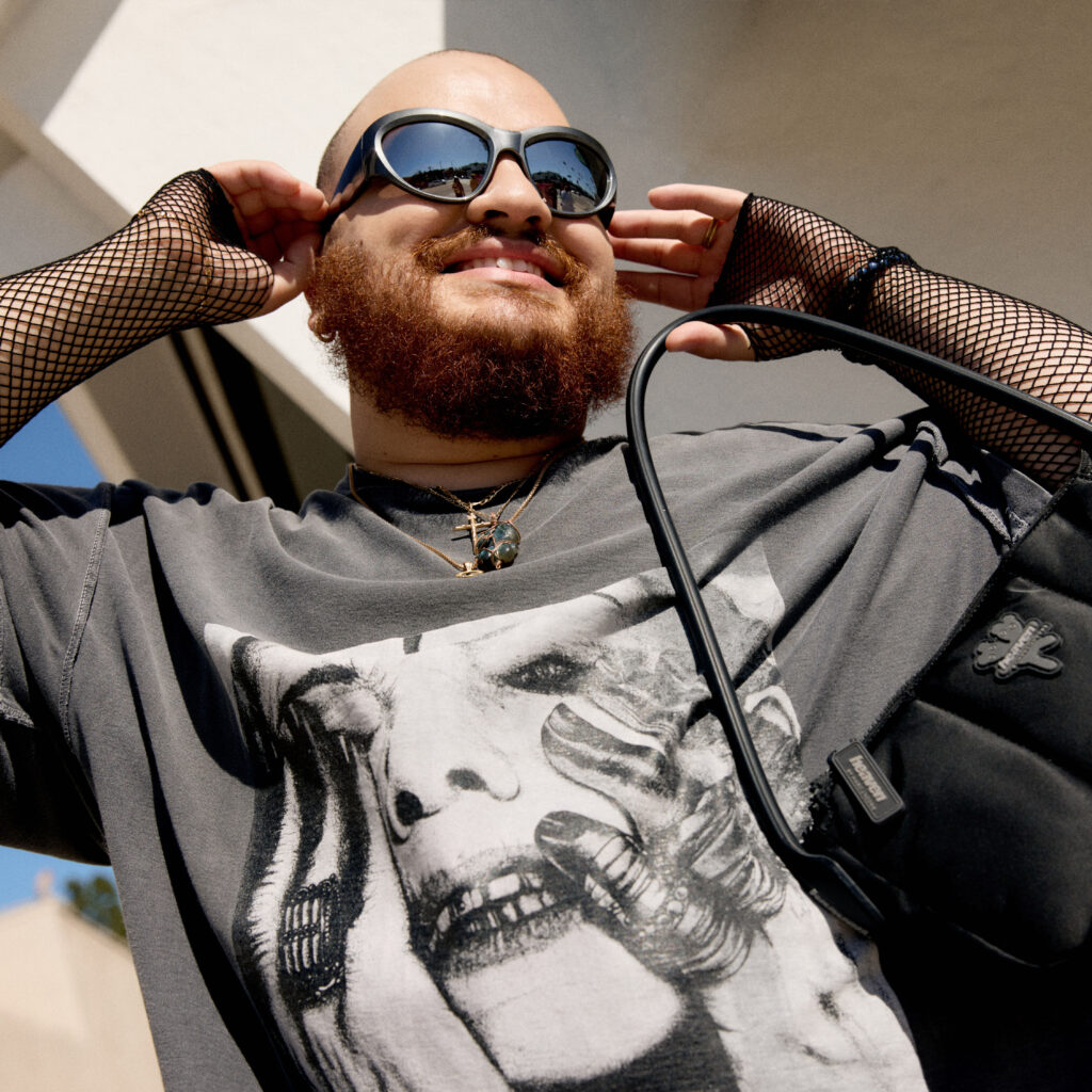 Nelson wearing sunglasses, fishnet sleeves and a graphic tee shirt